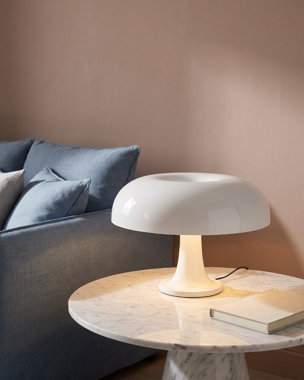 Beven table lamp in white lit on a side table beside a blue sofa
