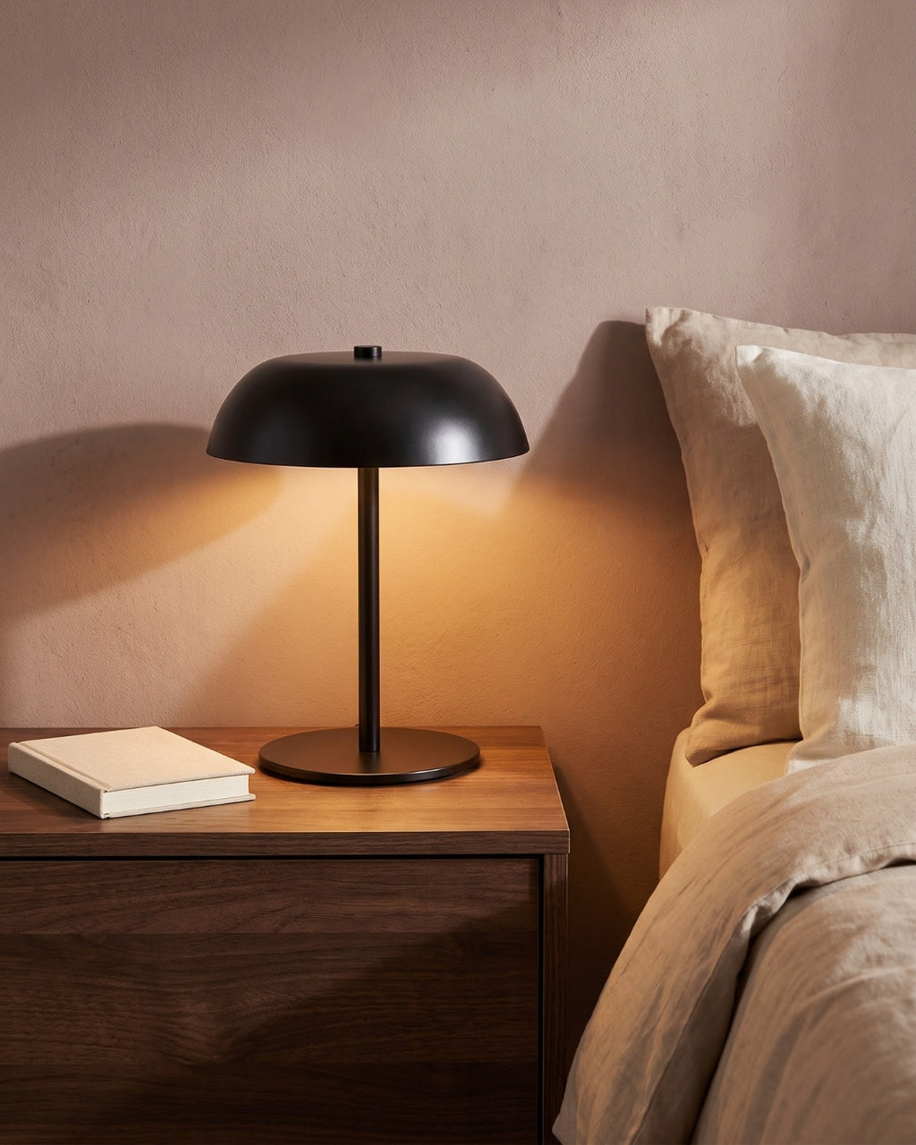 Gavetti table lamp in black lit on a nightstand beside a bed