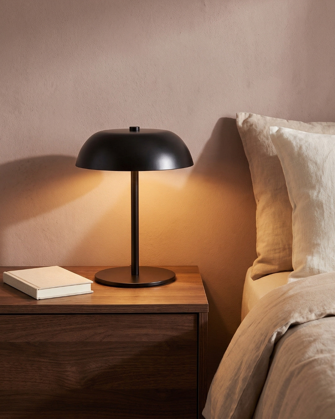 Gavetti table lamp in black lit on a nightstand beside a bed