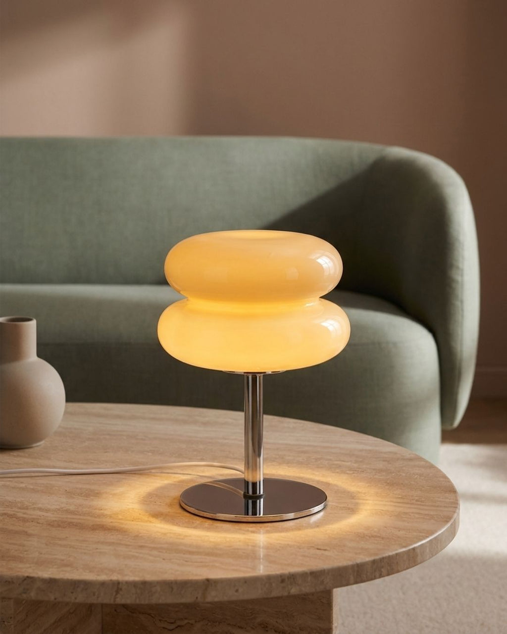Olvetti table lamp in cream lit on a coffee table in soft light