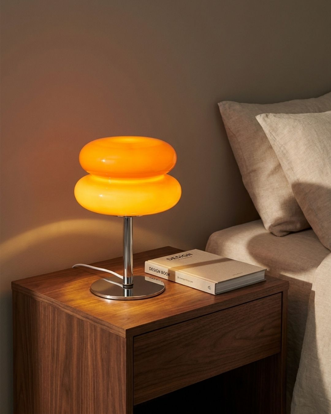 Olvetti table lamp in orange lit on a nightstand at night